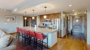 Una cocina moderna con una isla central, taburetes de bar, electrodomésticos de acero inoxidable y armarios de madera.
