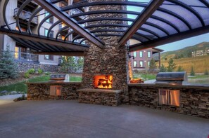 Ein Steinkamin mit Feuer, ein Grill und ein überdachter Außenbereich mit Metalldachkonstruktion.