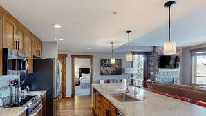 Una cocina moderna con armarios de madera, electrodomésticos de acero inoxidable, una isla grande con un lavamanos y una chimenea de piedra.