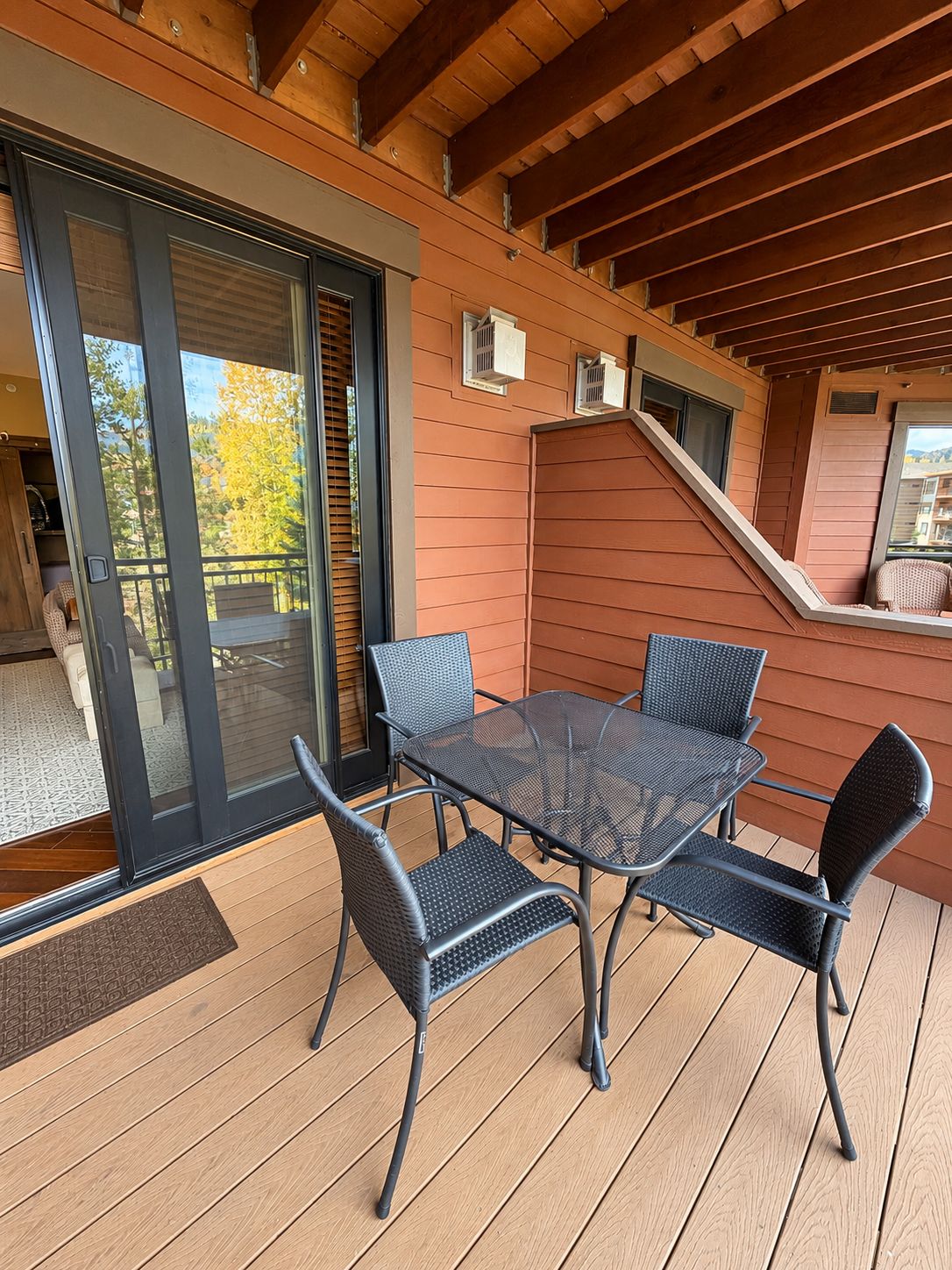 Un espacio al aire libre cubierto con mesa y sillas, un ventanal corredero y una terraza de madera.
