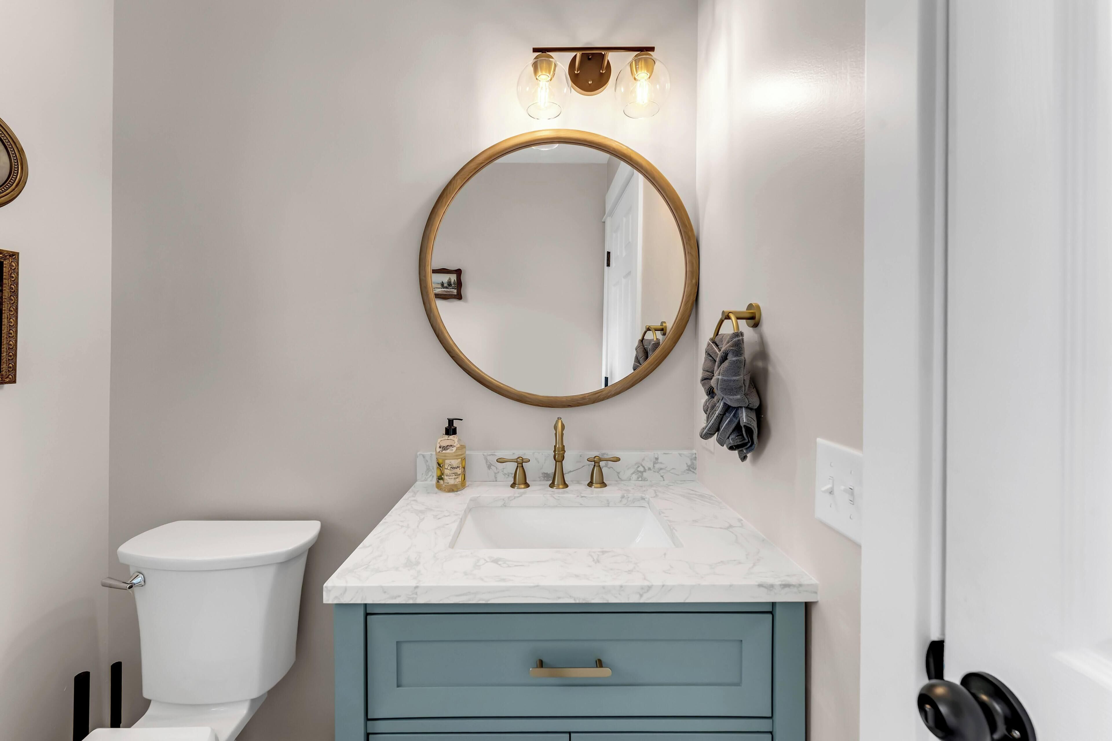 Un bagno con il water, un lavabo con piano in marmo, un armadietto blu, uno specchio rotondo con cornice dorata e un porta asciugamani.