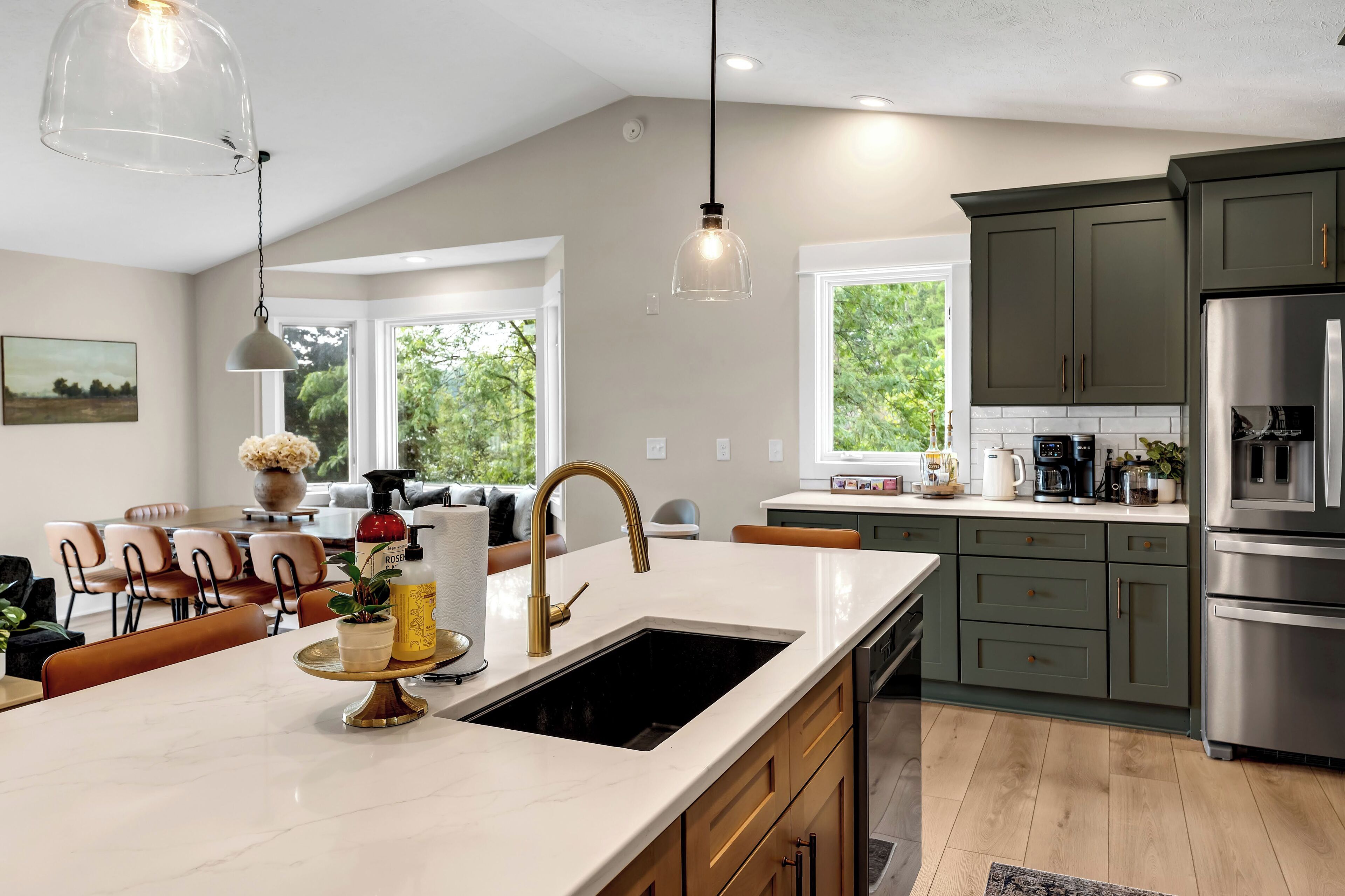 A modern kitchen with a large island, stainless steel appliances, and a dining area with a view of greenery.