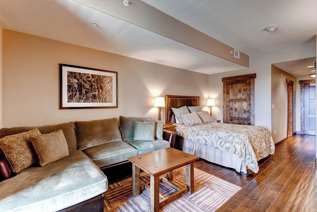 A room with a sofa, a bed, a wooden table, and a framed picture on the wall.