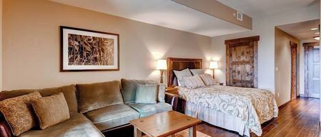 A room with a sofa, a bed, a wooden table, and a framed picture on the wall.