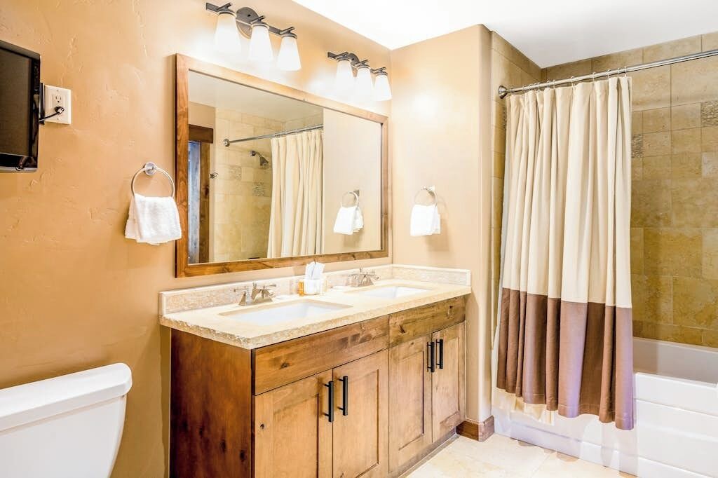 Ein Badezimmer mit einem Holzbadschränken, zwei Waschbecken, einem großen Spiegel und einer Duschvorhang.