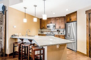 A kitchen with wooden cabinets, stainless steel appliances, and a central island with bar stools. - Luxurious condo w/ private balcony & shared pool, hot tubs, game room & fitness (Steamboat Springs)
