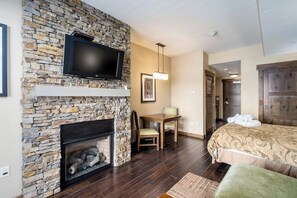Ein Hotelzimmer mit Kamin aus Stein, einem an der Wand befestigten Fernseher, einem Bett mit gemustertem Überwurf und einem Holztisch mit Stuhl.