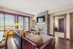 Ein Wohnzimmer mit Kamin aus Stein, einer Couch, einem Fernseher und großen Fenstern.