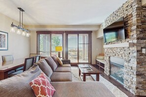Ein Wohnzimmer mit Kamin aus Stein, einem großen Flachbildfernseher und einem Essbereich mit Tisch und Stühlen.