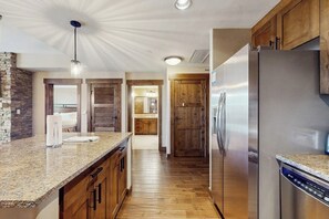 Eine moderne Küche mit Granitarbeitsplatte, Holzschränken, einem Edelstahlkühlschrank und einem Geschirrspüler.