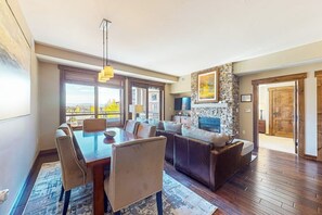 A spacious living area with a dining table, sofas, a stone fireplace, and large windows. - Gorgeous posh condo w/shared pool, hot tubs, fitness, game room & more (Steamboat Springs)