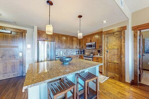 A kitchen with wooden cabinets, granite countertops, stainless steel appliances, and pendant lighting. - Gorgeous posh condo w/shared pool, hot tubs, fitness, game room & more (Steamboat Springs)