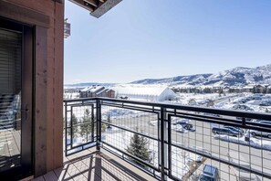 Ein Balkon mit Blick auf eine verschneite Landschaft, einen Parkplatz und Gebäude in der Ferne.