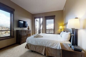 Ein Hotelzimmer mit Bett, Kommode, Fernseher, Lampe und Blick auf die Stadt.