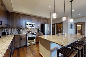 Eine moderne Küche mit Granit-Arbeitsplatten, Edelstahlgeräten, Holzschränken und Pendelleuchten.