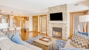 Ein modernes Wohnzimmer mit Kamin aus Stein, einem Flachbildfernseher und einem Essbereich mit Holzschränken und Pendelleuchten.