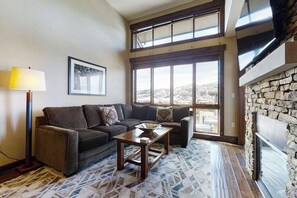 Ein Wohnzimmer mit einer Couch, einem Couchtisch, einer Lampe, einem Kamin und großen Fenstern mit Ausblick.