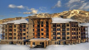 Een hotel met meerdere verdiepingen, een gevel van natuursteen, balkons en uitzicht op besneeuwde bergen.