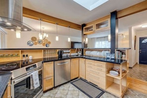 A modern kitchen with a skylight, stainless steel appliances, wooden cabinets, and a black countertop. - King Bed, AC, 75 min Banff, Newly Renovated (Calgary)