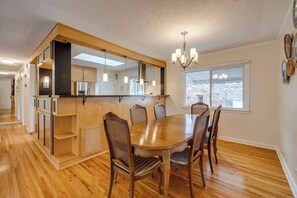 A dining area with a wooden table and chairs, a chandelier, and a large window with blinds. - King Bed, AC, 75 min Banff, Newly Renovated (Calgary)