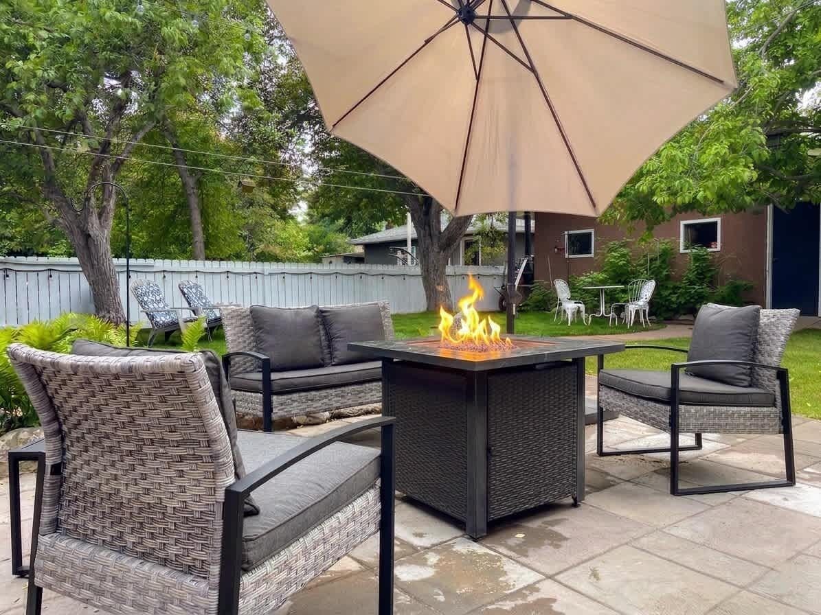 Um pátio externo com uma mesa quadrada, quatro cadeiras e um grande guarda-sol.