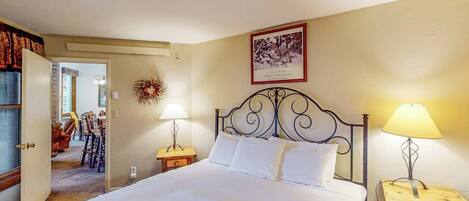 Quarto com cama, duas luminárias de cabeceira, um quadro na parede e uma porta que dá para outro cômodo.