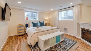 A bedroom with a bed, bedside tables, a bench, a fireplace, and windows. - King Bed, 75 min Banff, AC Backyard Chickens (Calgary)