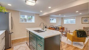 A modern kitchen with a central island, a dining area with a table and chairs, and a living room with a sofa. - King Bed, 75 min Banff, AC Backyard Chickens (Calgary)