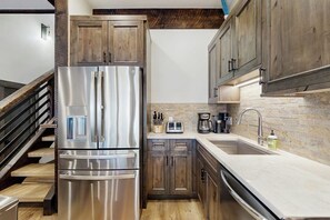 A kitchen with wooden cabinets, a stainless steel refrigerator, a sink, and a coffee maker. - Large, creekside condo w/ shared hot tubs - across the street from resort trails (Steamboat Springs)
