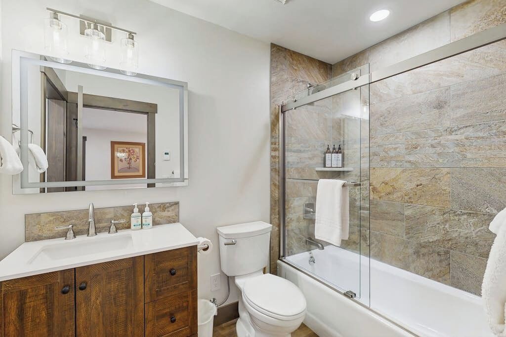 A modern bathroom with a glass-enclosed shower, a white toilet, and a wooden vanity with a mirror.