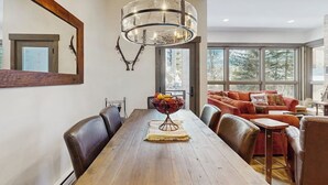 Een eetgedeelte met een houten tafel, stoelen, een kroonluchter en een bank met kussens.