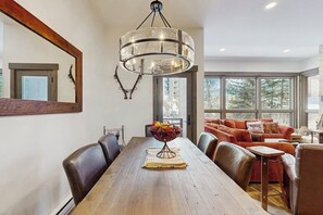 A dining area with a wooden table, chairs, a chandelier, and a sofa with cushions. - Large, creekside condo w/ shared hot tubs - across the street from resort trails (Steamboat Springs)