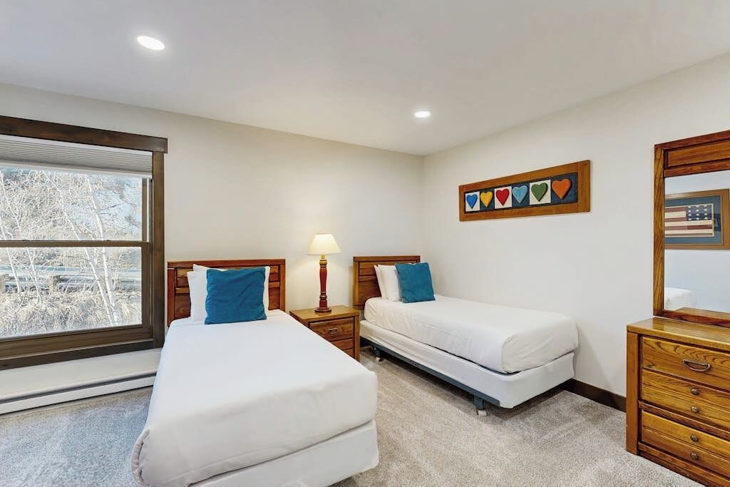 Une chambre d’hôtel avec deux lits, une fenêtre avec des stores, une commode en bois et un élément décoratif mural.