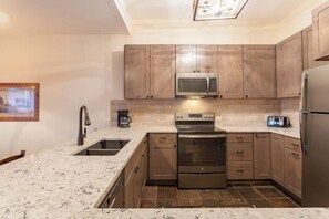 Eine Küche mit Holzschränken, einem Edelstahlkühlschrank, einer Mikrowelle, einem Backofen und einem Spülbecken.