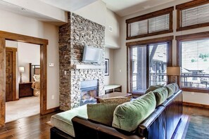 Ein Wohnzimmer mit Kamin aus Stein, Holzmöbeln und großen Fenstern.