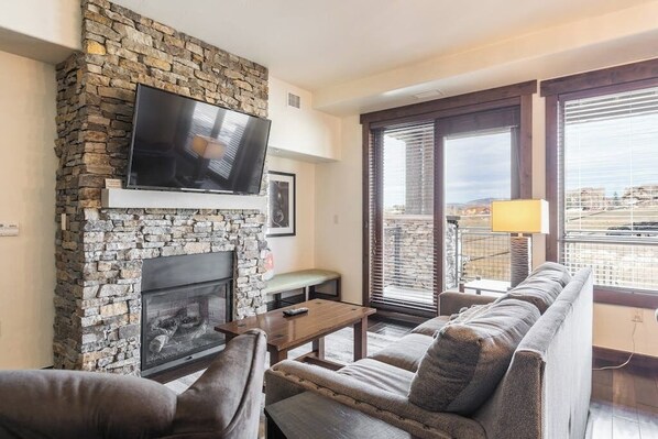 Ein Wohnzimmer mit Kamin aus Stein, einem Flachbildfernseher, einer Couch und einem Balkon mit Blick.