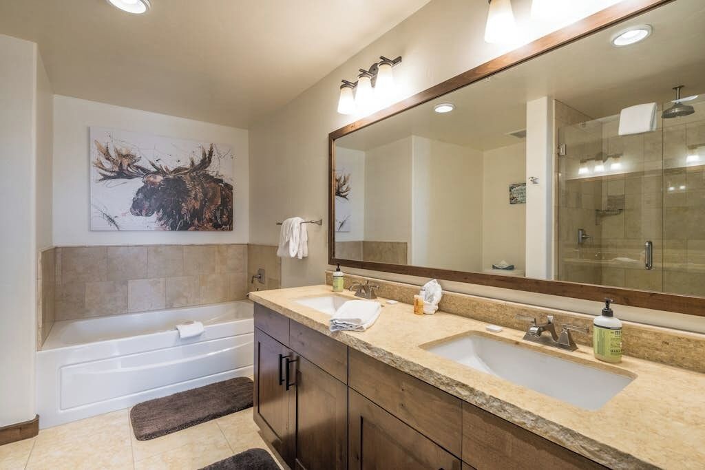 Un baño con una bañera, dos lavamanos, un espejo grande y una obra de arte en la pared de un alce.