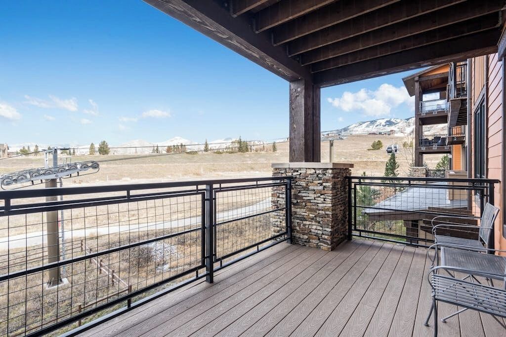 A wooden deck with a stone wall, metal railing, and a table with chairs.