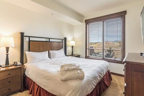 Ein ordentlich bezogenes Bett mit einem hölzernen Kopfteil, zwei Nachttischlampen, einem Telefon und einem Fenster mit Jalousien.
