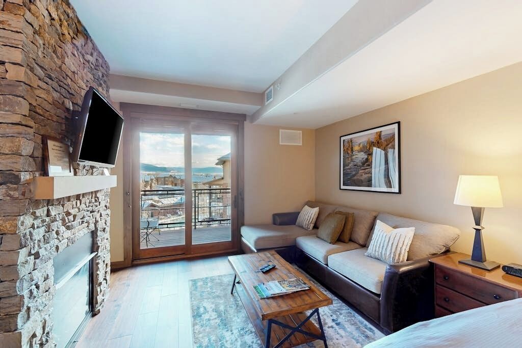 Habitació d'hotel amb paret de pedra, televisió de pantalla plana, sofà, taula de cafè, làmpada i balcó amb vistes.