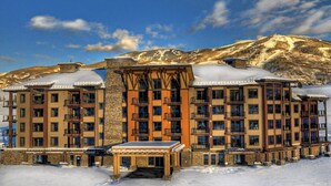 Um hotel com vários andares, varandas, área de estar coberta ao ar livre e montanhas ao fundo.
