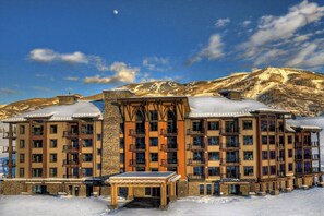 Ein mehrstöckiges Hotel mit Balkonen, einer überdachten Außenlounge und einer Bergkulisse im Hintergrund.