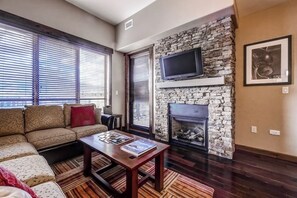 A living room with a stone fireplace, a flat-screen TV, a sofa, and a coffee table. - Impressive condo w/private balcony, gondola access, shared pool and hot tubs (Steamboat Springs)