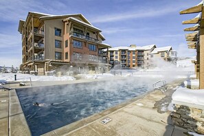 A pool with steam rising, surrounded by snow-covered buildings. - Perfect upscale studio w/private balcony, gondola access & shared hot tubs, pool (Steamboat Springs)