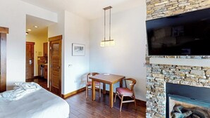 Ein Zimmer mit einem Bett, einem Esstisch mit Stühlen, einem Kamin und einem an der Wand befestigten Fernseher.