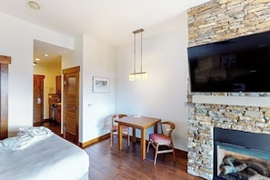 A room with a bed, a dining table with chairs, a fireplace, and a television mounted on the wall. - Perfect upscale studio w/private balcony, gondola access & shared hot tubs, pool (Steamboat Springs)