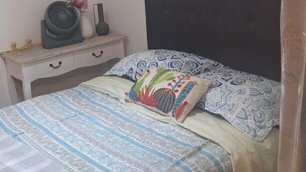 Quarto com uma cama, mesa de cabeceira com abajur, relógio de parede e um quadro emoldurado.
