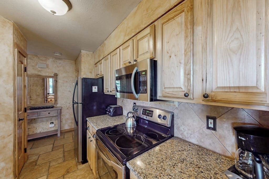 Una cocina con armarios de madera, un refrigerador de acero inoxidable, un microondas, una estufa y una cafetera.