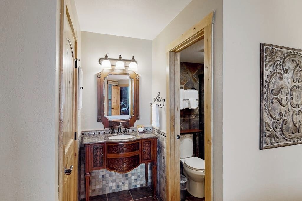 Ein Badezimmer mit einem Holzauszug, einem großen, beleuchteten Spiegel, einer Toilette und einer Wanddekoration.