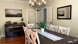 A dining room with a dark wooden table, white chairs, a chandelier, a piano, and framed artwork on the walls. - Lovely 4-bed/2-bath house with plenty of space for large groups (Moscow)